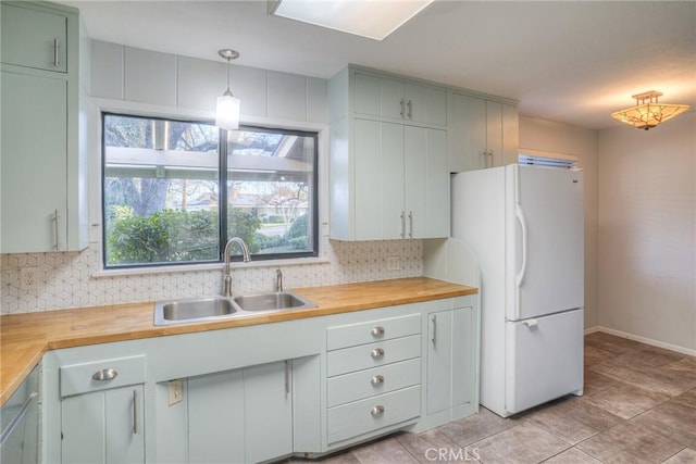 kitchen with butcher block counters, decorative backsplash, white refrigerator, pendant lighting, and sink