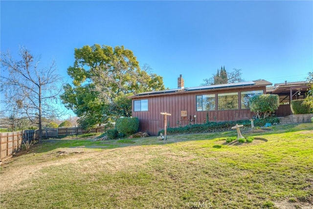 exterior space with board and batten siding, a fenced backyard, a lawn, and a chimney