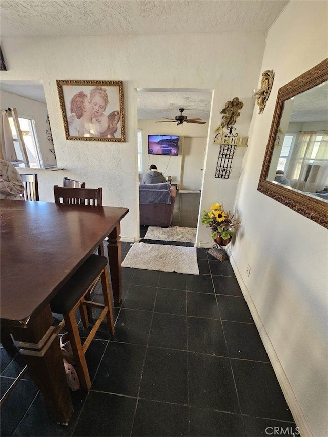 dining space with a textured ceiling, dark tile patterned flooring, a ceiling fan, and baseboards