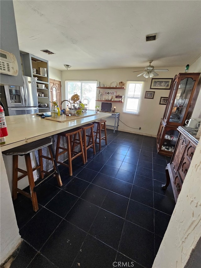 kitchen with a breakfast bar area, visible vents, ceiling fan, and stainless steel fridge with ice dispenser