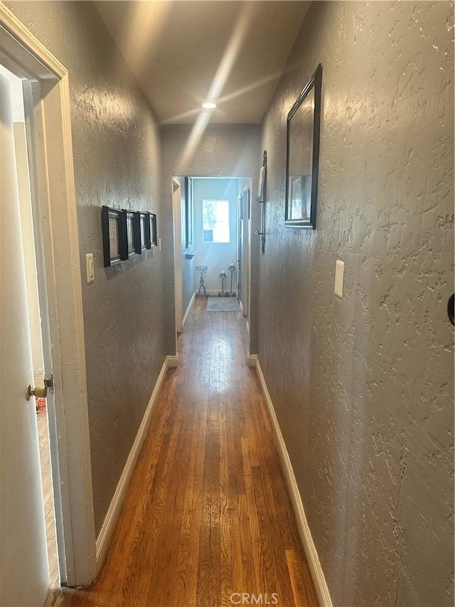 hall featuring baseboards, wood finished floors, and a textured wall