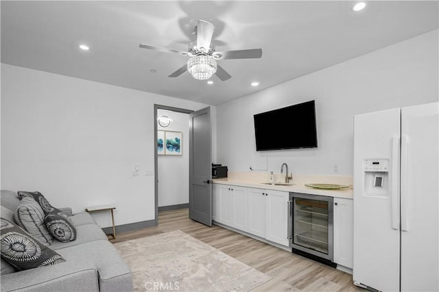 bar featuring sink, light hardwood / wood-style flooring, white fridge with ice dispenser, beverage cooler, and white cabinets