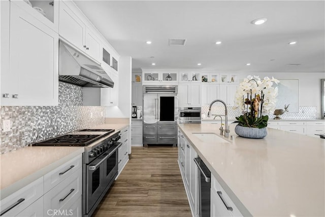 kitchen featuring dark wood-type flooring, sink, high quality appliances, white cabinets, and wall chimney range hood