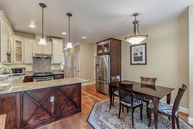 kitchen with kitchen peninsula, appliances with stainless steel finishes, tasteful backsplash, and decorative light fixtures