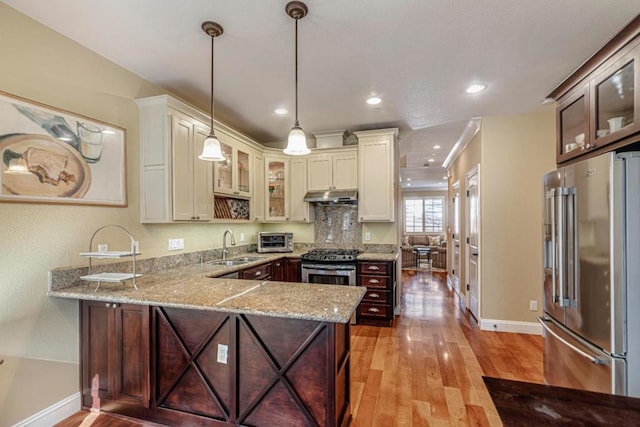 kitchen featuring decorative light fixtures, light stone countertops, kitchen peninsula, and stainless steel appliances