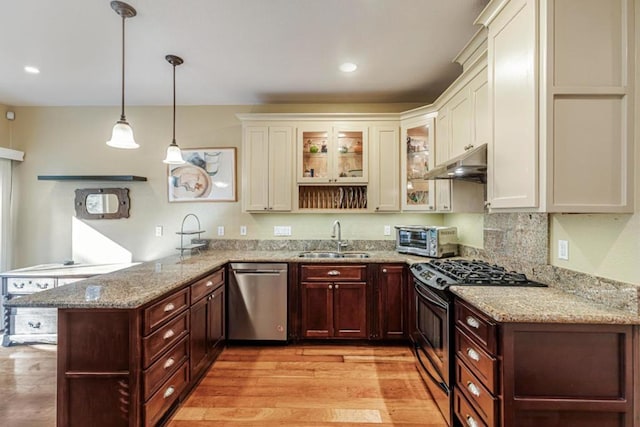 kitchen featuring kitchen peninsula, stainless steel appliances, hanging light fixtures, light stone countertops, and sink