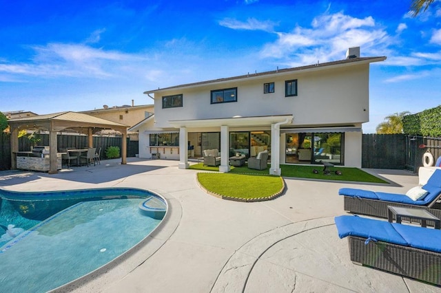 rear view of property with outdoor lounge area, an outdoor kitchen, a fenced in pool, a gazebo, and a patio area