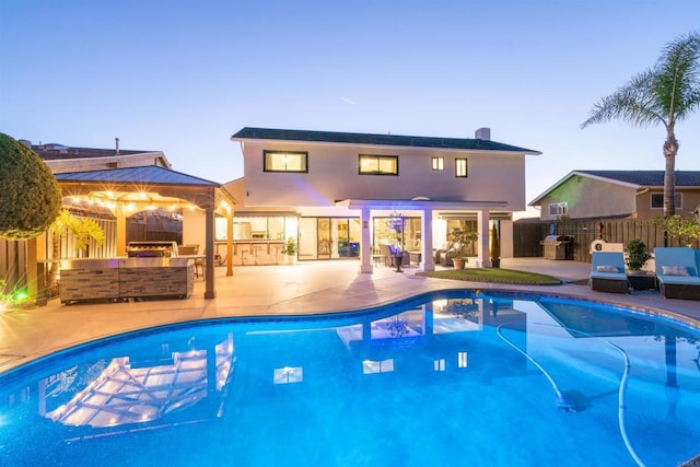 pool at dusk featuring exterior kitchen and a patio area