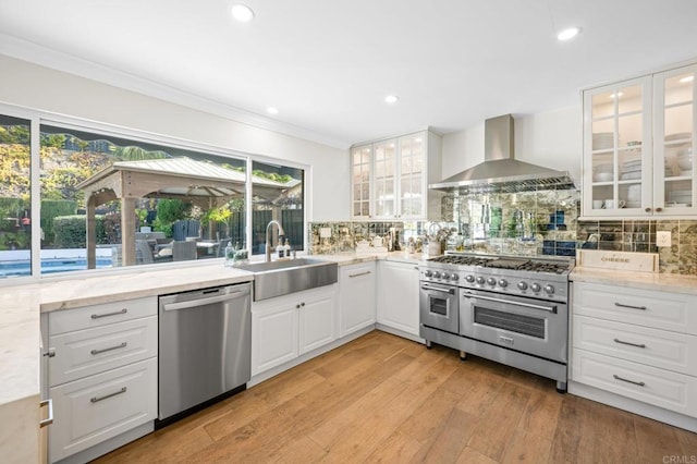 kitchen with sink, appliances with stainless steel finishes, a wealth of natural light, wall chimney range hood, and white cabinets