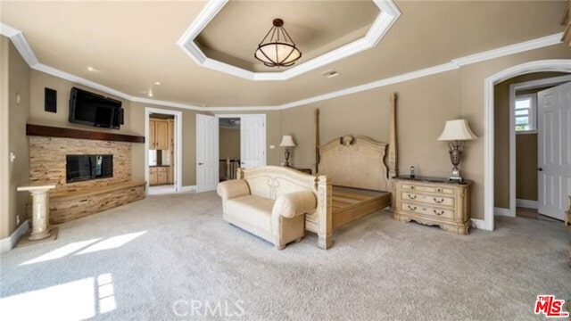 carpeted bedroom with a tray ceiling, crown molding, and a fireplace