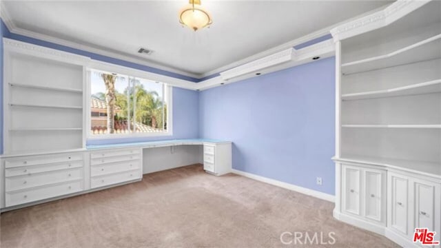 unfurnished office with built in desk, light colored carpet, and crown molding