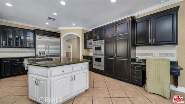 kitchen featuring appliances with stainless steel finishes, white cabinetry, an island with sink, backsplash, and light tile patterned flooring