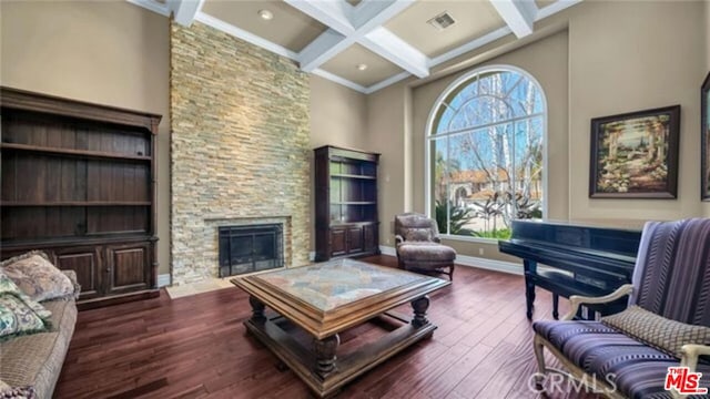 living room featuring dark wood-type flooring, beam ceiling, a stone fireplace, and coffered ceiling