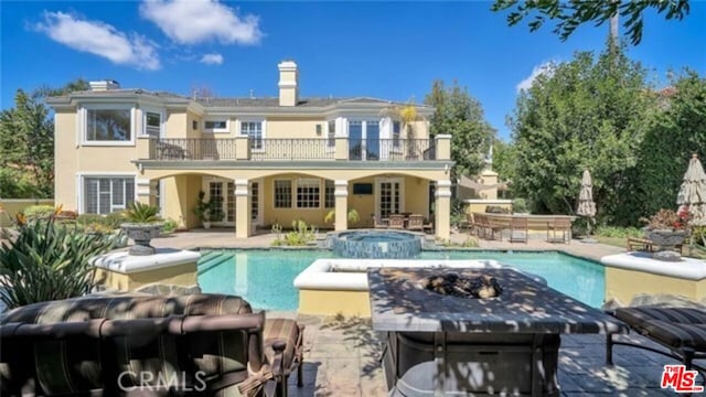 rear view of property featuring a pool with hot tub, a balcony, and a patio