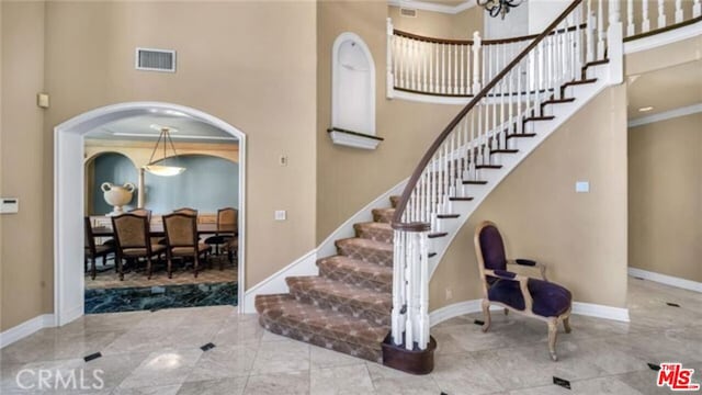 staircase featuring a high ceiling, ornamental molding, and a notable chandelier