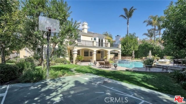 rear view of house with a patio area, a lawn, basketball court, and a balcony