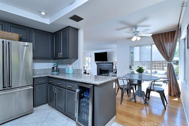 kitchen with high quality fridge, a fireplace, wine cooler, kitchen peninsula, and light stone counters