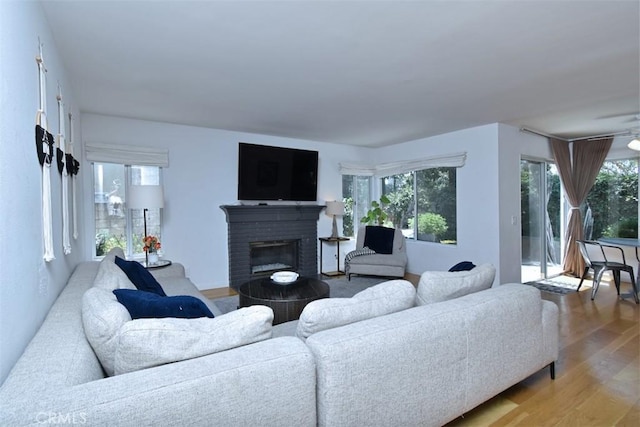 living room with a brick fireplace, a wealth of natural light, and hardwood / wood-style flooring