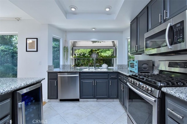 kitchen with wine cooler, a raised ceiling, sink, appliances with stainless steel finishes, and light stone counters