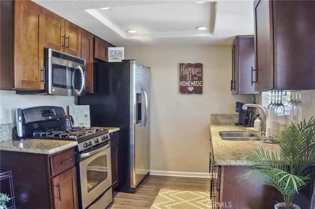 kitchen with light stone countertops, sink, appliances with stainless steel finishes, and light wood-type flooring