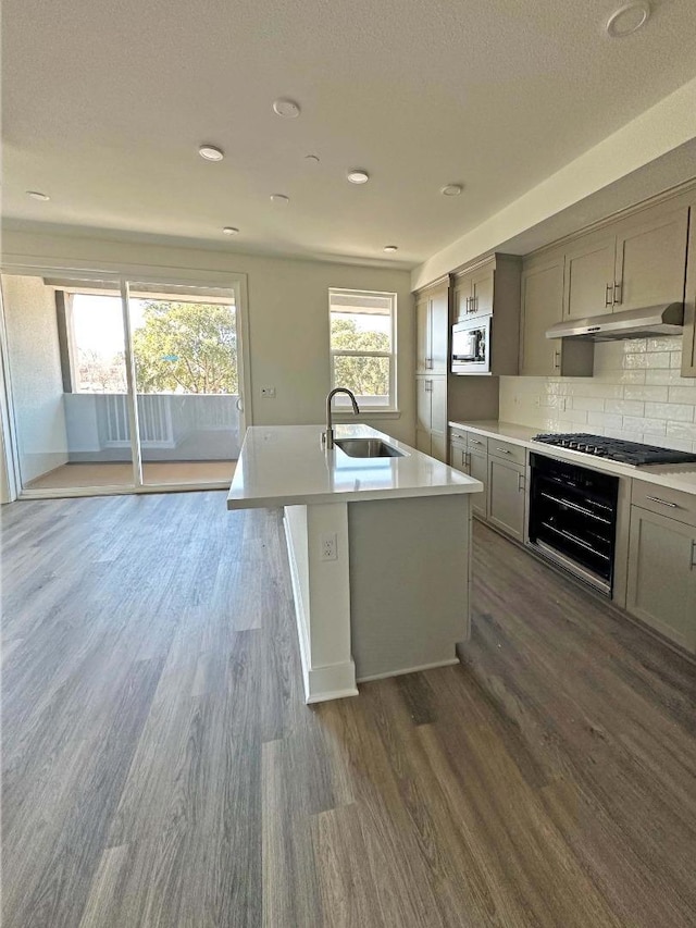 kitchen with sink, dark hardwood / wood-style flooring, stainless steel gas cooktop, an island with sink, and built in microwave