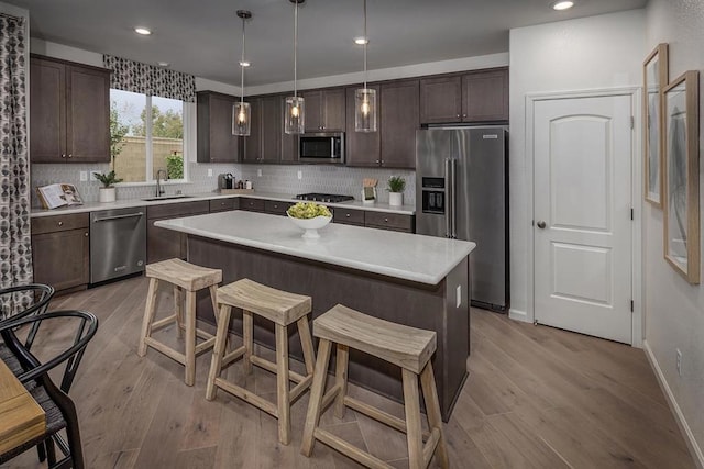 kitchen with light hardwood / wood-style floors, stainless steel appliances, hanging light fixtures, a kitchen island, and sink