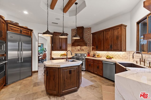 kitchen with sink, pendant lighting, high end appliances, an island with sink, and beamed ceiling