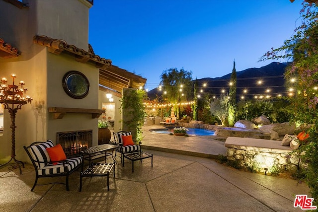 patio terrace at dusk with a mountain view and exterior fireplace