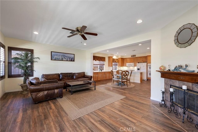 living room with ceiling fan, a tiled fireplace, and dark hardwood / wood-style floors