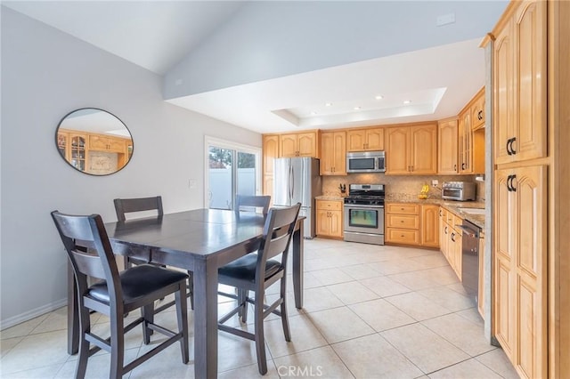 kitchen with appliances with stainless steel finishes, tasteful backsplash, a tray ceiling, light stone countertops, and light tile patterned flooring