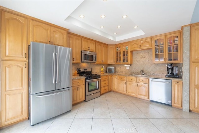 kitchen with sink, appliances with stainless steel finishes, backsplash, light stone countertops, and a raised ceiling