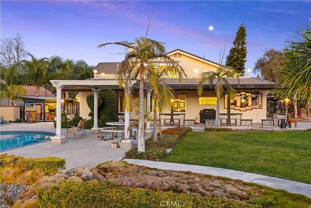 back house at dusk featuring a patio area and a yard