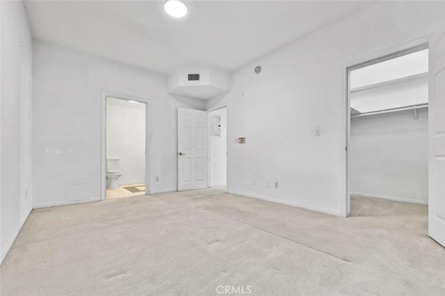 unfurnished bedroom featuring light colored carpet, connected bathroom, and a closet