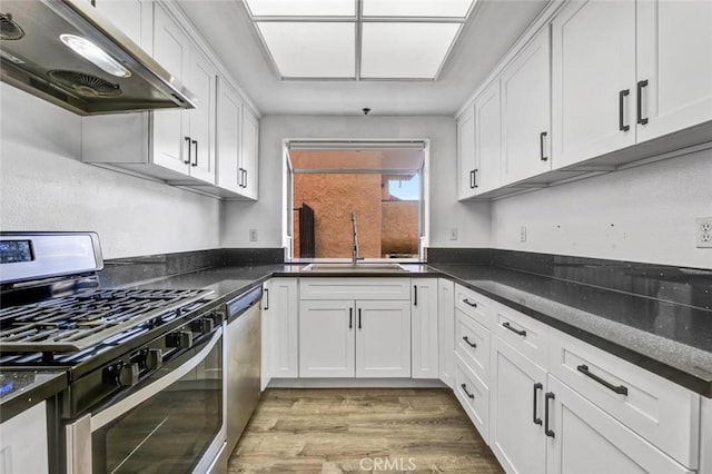 kitchen with dark stone countertops, light hardwood / wood-style floors, sink, stainless steel appliances, and white cabinets