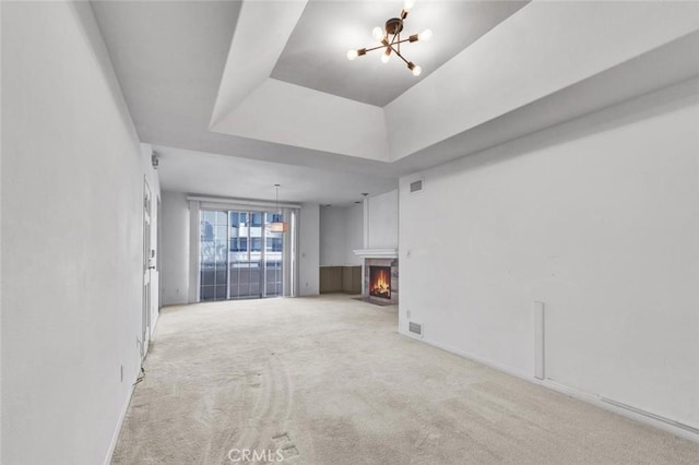 unfurnished living room with light colored carpet, a tray ceiling, and a chandelier