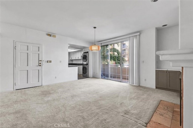 unfurnished living room featuring stacked washer / dryer and carpet