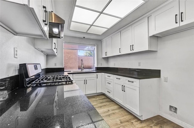 kitchen featuring sink, light wood-type flooring, white cabinets, dark stone counters, and gas range