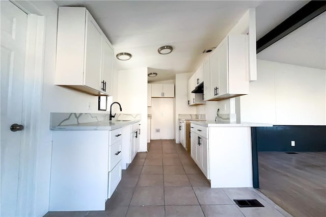 kitchen with dark tile patterned floors, beam ceiling, white cabinets, and sink