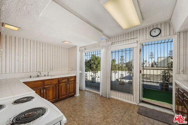 kitchen with tile counters, white electric range, sink, and a textured ceiling