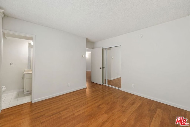 unfurnished bedroom with a closet, a textured ceiling, connected bathroom, and light hardwood / wood-style flooring