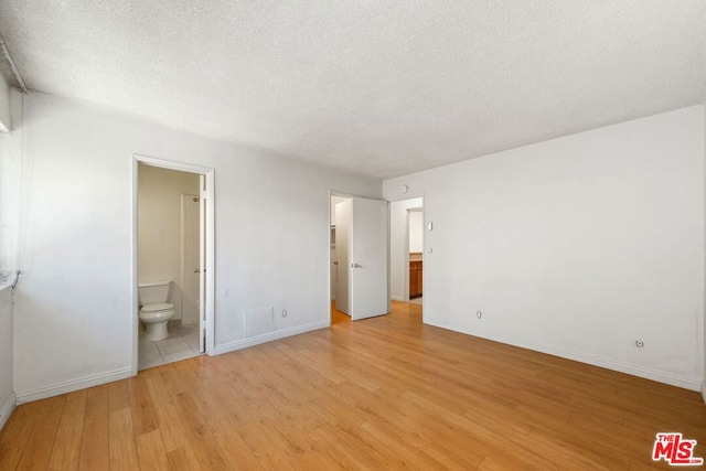 unfurnished bedroom featuring a textured ceiling, connected bathroom, and light hardwood / wood-style flooring