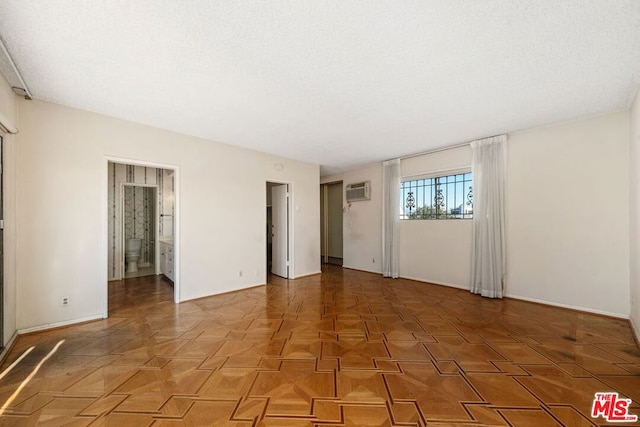 empty room with parquet floors, a textured ceiling, and a wall unit AC