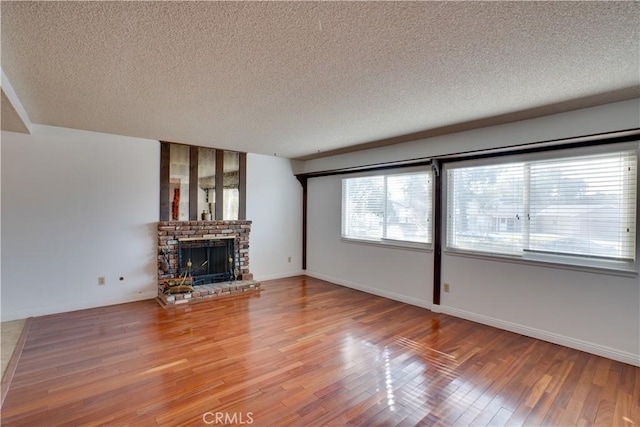 unfurnished living room featuring wood-type flooring, a brick fireplace, and a textured ceiling