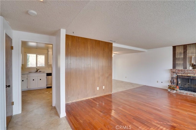 unfurnished living room featuring a fireplace, sink, wood walls, and a textured ceiling