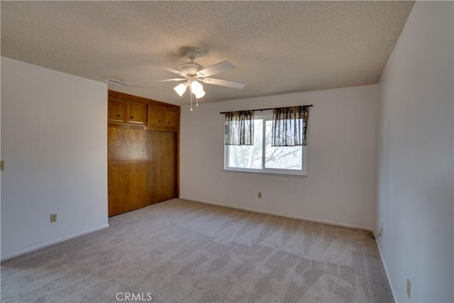 unfurnished bedroom featuring ceiling fan, light colored carpet, a closet, and a textured ceiling