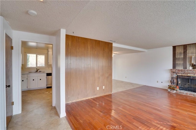 unfurnished living room featuring a brick fireplace, sink, wood walls, and a textured ceiling