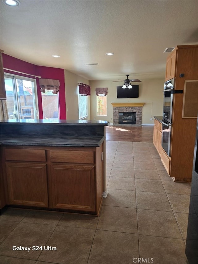 kitchen featuring tile patterned flooring, ceiling fan, a stone fireplace, and double oven