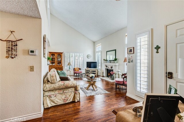living room featuring a brick fireplace, high vaulted ceiling, baseboards, and wood finished floors