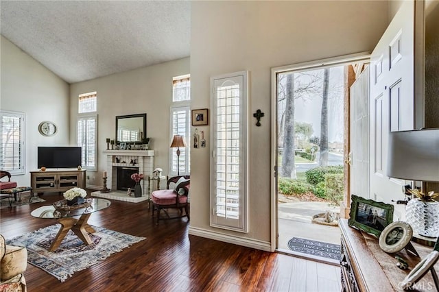foyer featuring high vaulted ceiling, baseboards, a textured ceiling, a brick fireplace, and wood finished floors
