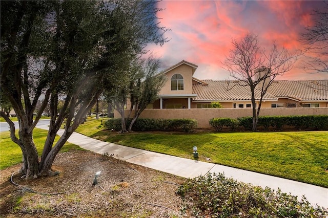 view of front of home featuring a tile roof, stucco siding, fence, and a yard